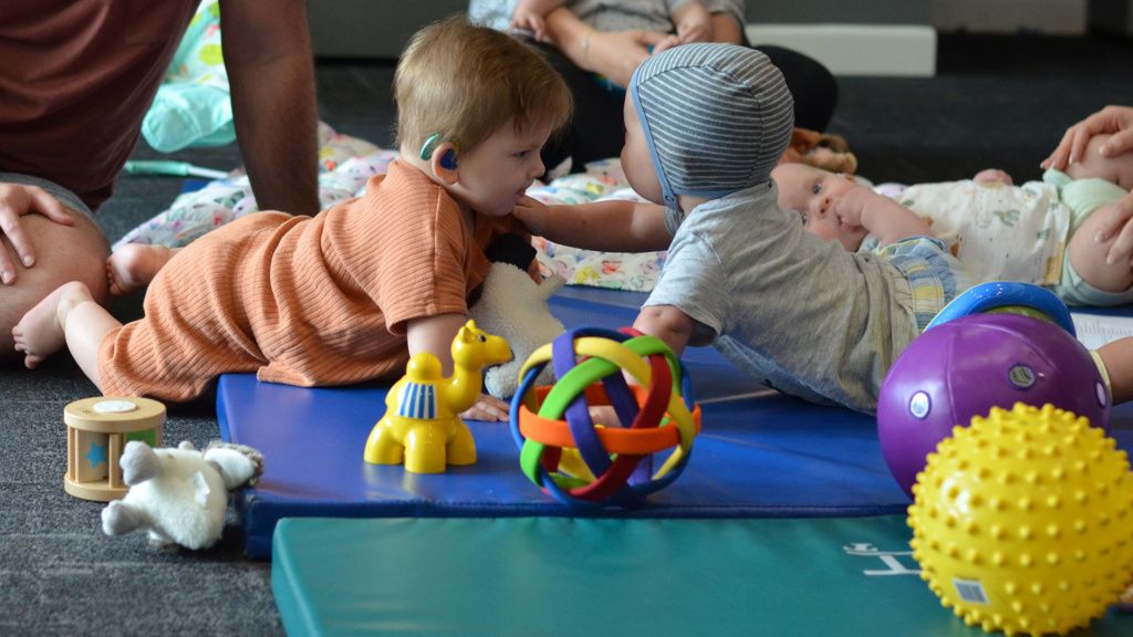 Two Babies Reaching For Each Other Surrouneded By Toys