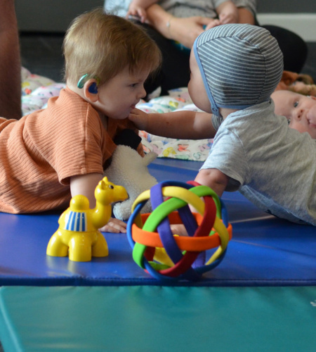 Two Babies Reaching For Each Other Surrouneded By Toys
